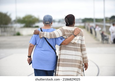 Older Women Walking Arm And Arm Outside On A Boardwalk