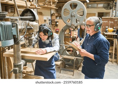 An older worker guides a young apprentice in a carpentry workshop, highlighting teamwork, training, and skill development. The image captures a collaborative work environment with various woodworking 