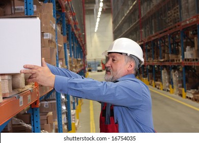 Older Worker In Uniform Putting Heavy Box On  Shelf In Warehouse