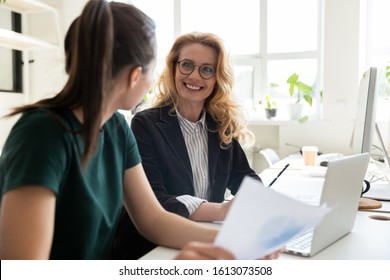 Older and young office worker women workmates sit at shared desk working together do statistical analysis using pc app, financial report charts and data, friendly mates common task, mentoring concept