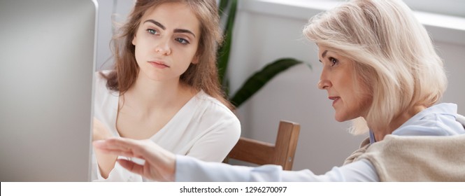 Older and younger women colleagues working on new project discuss online app point on pc screen mentor teach help intern explain corporate software, teamwork concept close up banner for website header - Powered by Shutterstock