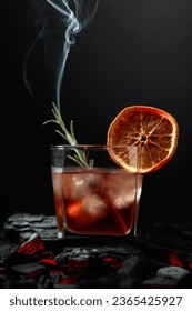 Old-fashioned cocktail with ice, dried orange slice, and rosemary. Whiskey with rosemary and beautiful swirls of smoke on a black background. - Shutterstock ID 2365425927