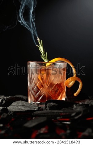 Old-fashioned cocktail with ice, orange peel, and rosemary. Whiskey with a burning twig of rosemary on a dark background.