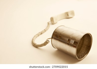 Old-fashioned communication device made from a tin can and telephone cord rests on a plain surface showcasing creativity in communication methods