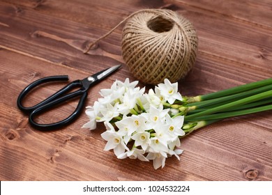 Old-fashioned florist scissors with a bunch of white narcissi and a ball of twine, gathered on a wooden table