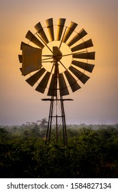Old-fashioned and low tech waterpump windmill in rural farm area against a dramatic sunset with orange and magenta colors. Wind Power providing renewable and green energy no carbon emissions. 
