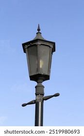 Old-fashioned street lamp light on a black metal pole against a clear blue sky