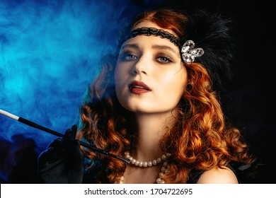 Old-fashioned woman dressed in style of Flappers posing with cigarette in mouthpiece on dark background with neon light. Roaring twenties, retro, party, fashion concept