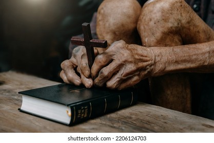 Oldman sitting and studying the scriptures.The  wooden cross in the hands. Christian education concepts The Holy Scriptures open and pray to God.