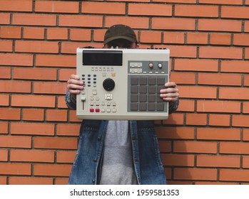 An old-school ' 90s drum machine in the hands of a beatmaker against a brick wall. Retro Digital Musical Instrument for Hip Hop Producers and Beatmakers