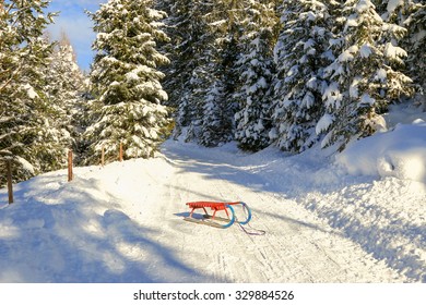 An Old-styled Rodel (Toboggan) In Red And Blue On Snowy Path In The Forest In Austria