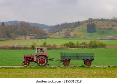 Oldtimer vintage agricultural tractor towing a trailer on a country road.