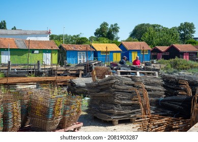 Oleron Island harbour, Charente Maritime, France June 7th 2014 : Two fishermen talking amongst colourful oyster farming cabins and foreground shellfish fishing equipment