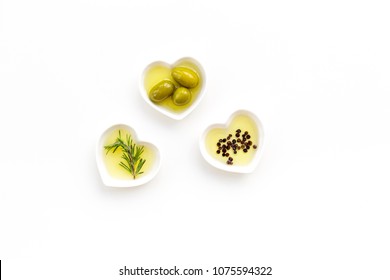 Olive oil as famous product of mediterranean cuisine. Heart shaped bowls with olive oil with green olives, rosemary and black pepper inside on white background top view copy space