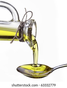 Olive Oil Flowing From Carafe Into The Spoon Isolated On A White.