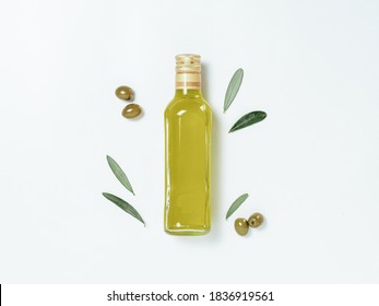 Olive Oil Glass Bottle Mock Up. Top View Of Clear Glass Bottle With Olive Oil On White Background With Green Olives And Fresh Green Olive Tree Leaves. Copy Space.