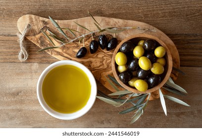 Olive oil and green and black olives in a wooden bowl top view. Olive oil and green and black olives in a wooden bowl on olive wood board with olive leaves all around taken from above - Powered by Shutterstock