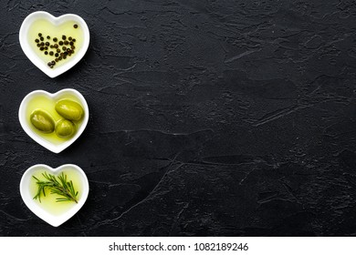 Olive oil as healthy diet product. Heart shaped bowls with olive oil with green olives, rosemary and black pepper inside on black background top view copy space