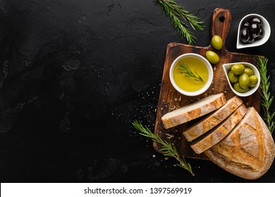Olive oil and olives in bowls, sliced bread and rosemary on cutting board over concrete background, top view, copy space