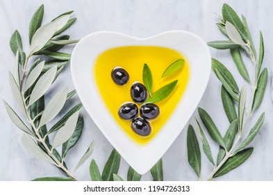 Olive oil and olives on white marble background.Heart shaped bowl with olive oil.