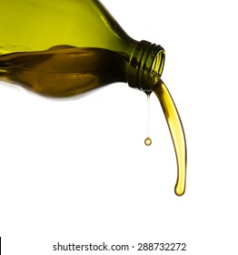 Olive oil pouring from green glass bottle, isolated against white background.