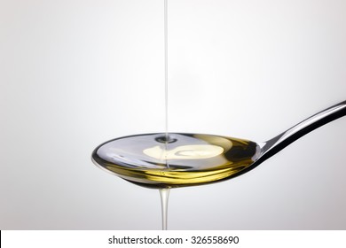 Olive Oil Pouring On Spoon Over White Background