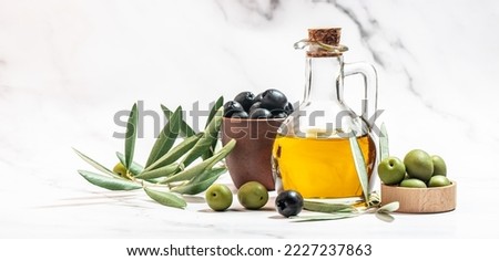 Olive oil in two glass containers and harvest olives berries in bowls on a light background. Long banner format.