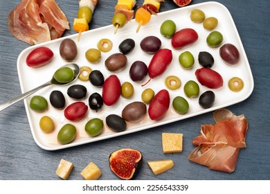 Olives of different varieties and colors a white plate. Cheese, olives, jamon and figs on a table. Flat lay. Blue background. - Powered by Shutterstock