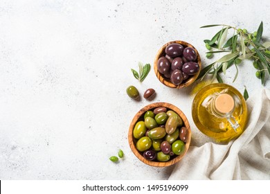 Olives In Wooden Bowls And Olive Oil Bottle On White Background. Top View With Copy Space.