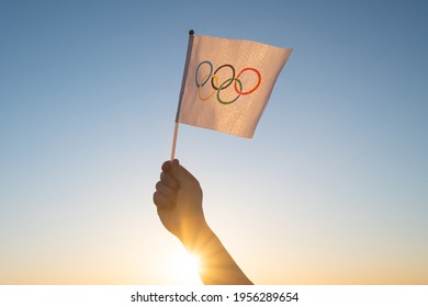 The Olympic flag, small in hand, flutters against the backdrop of blue sky and setting sun. Concept for Winter and Summer Olympic Games, 2021, 2022.