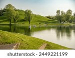 The Olympic Hill and the Olympic Lake with some pedal boats on it in the Olympic Park in Munich, Germany in spring. White and blue sky