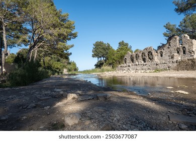 Olympos Turkey Ancient Ruins by the Stream ancient stone ruins beside a tranquil stream, surrounded by lush greenery and under a clear blue sky.  - Powered by Shutterstock