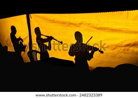 OLYMPUS DIGITAL CAMERAThis photo shows the silhouettes of a group of musicians seen from inside a tent-like structure. The backlighting creates a warm yellow background, making the musicians' silhouet