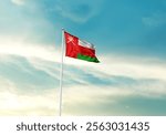 Oman flag is waving on a tall flagpole among the clouds. Oman national flag for independence day.