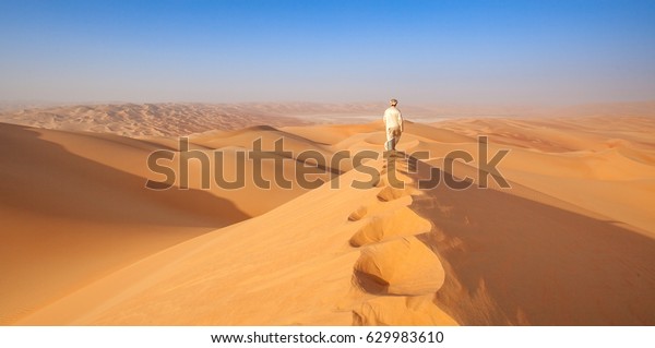 Omani Man\
walking over sand dune in the empty\
quarter