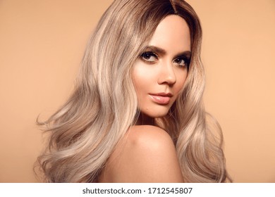 Ombre blond wavy hairstyle. Beauty fashion blonde woman portrait. Beautiful girl model with makeup, long healthy hair style posing isolated on studio beige background.