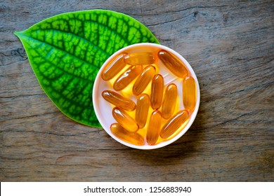 Omega 3 Fish Oil Pills Served With Green Leaf On The Wooden Table. Fish Oil Soft Gel Capsules On Leaf. Colorful Food Supplement Pill.