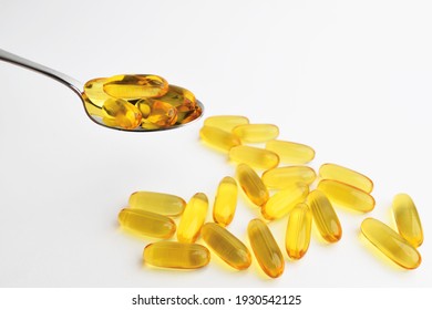 Omega 3 pills on spoon. Yellow vitamin, transparent yellow vitamin tablet with teaspoon. Cod liver oil. Gel capsules on white background space for text. 