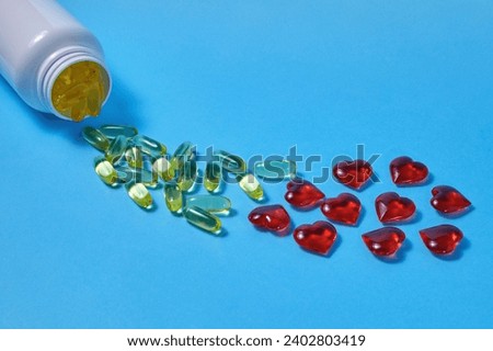 Omega 3 polyunsaturated fatty acids and red hearts pour out from a white plastic jar on a blue background. Prevention and treatment of atherosclerosis.