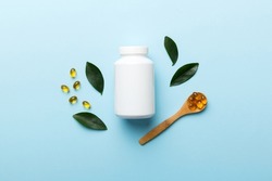 Omega-3 Capsules Lie In White Bottle On A Table With Green Leaves Background. Fish Oil Tablets. Biologically Active Additives. Omega 6, Omega 9, Vitamin A, E, D, Vitamin D3 Top View With Copy Space.