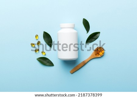 Omega-3 capsules lie in white bottle on a table with green leaves background. Fish oil tablets. Biologically active additives. omega 6, omega 9, vitamin A, E, D, vitamin D3 top view with copy space.