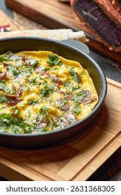 Omelet with cured meat and herbs in a cast iron skillet. This close-up shows a rustic, golden-yellow omelet freshly cooked in a cast-iron pan.