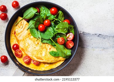 Omelet with fresh spinach and tomato salad in a frying pan on a gray table, top view. Breakfast food.