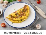 Omelet with fried mushrooms and fresh herbs in a plate on a concrete background. Delicious healthy breakfast. Top view. Copy space