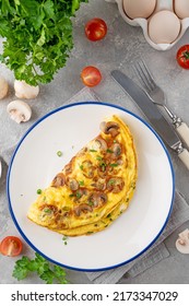 Omelet with fried mushrooms and fresh herbs in a plate on a concrete background. Delicious healthy breakfast. Top view. Copy space