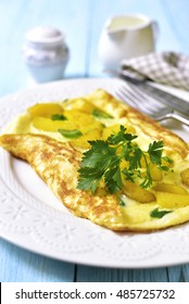Omelet stuffed with potato and cheese on a white plate on blue wooden background.