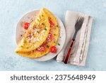 An omelet with tomato and parsley, eggs for breakfast, a healthy vegetarian dish with cheese, overhead flat lay shot with a fork