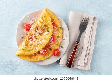 An omelet with tomato and parsley, eggs for breakfast, a healthy vegetarian dish with cheese, overhead flat lay shot with a fork