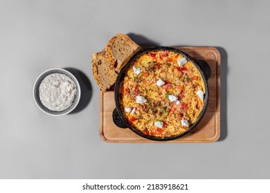 Omelet with tomatoes, paprika and goat cheese. Topped with a mixture of Italian herbs and microgreen pea sprouts. The omelet lies in a black iron frying pan. The frying pan stands on a square wooden b