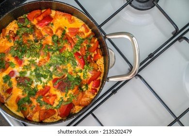 Omelette With Vegetables And Herbs In Black Frying Pan On White Stove. Top View